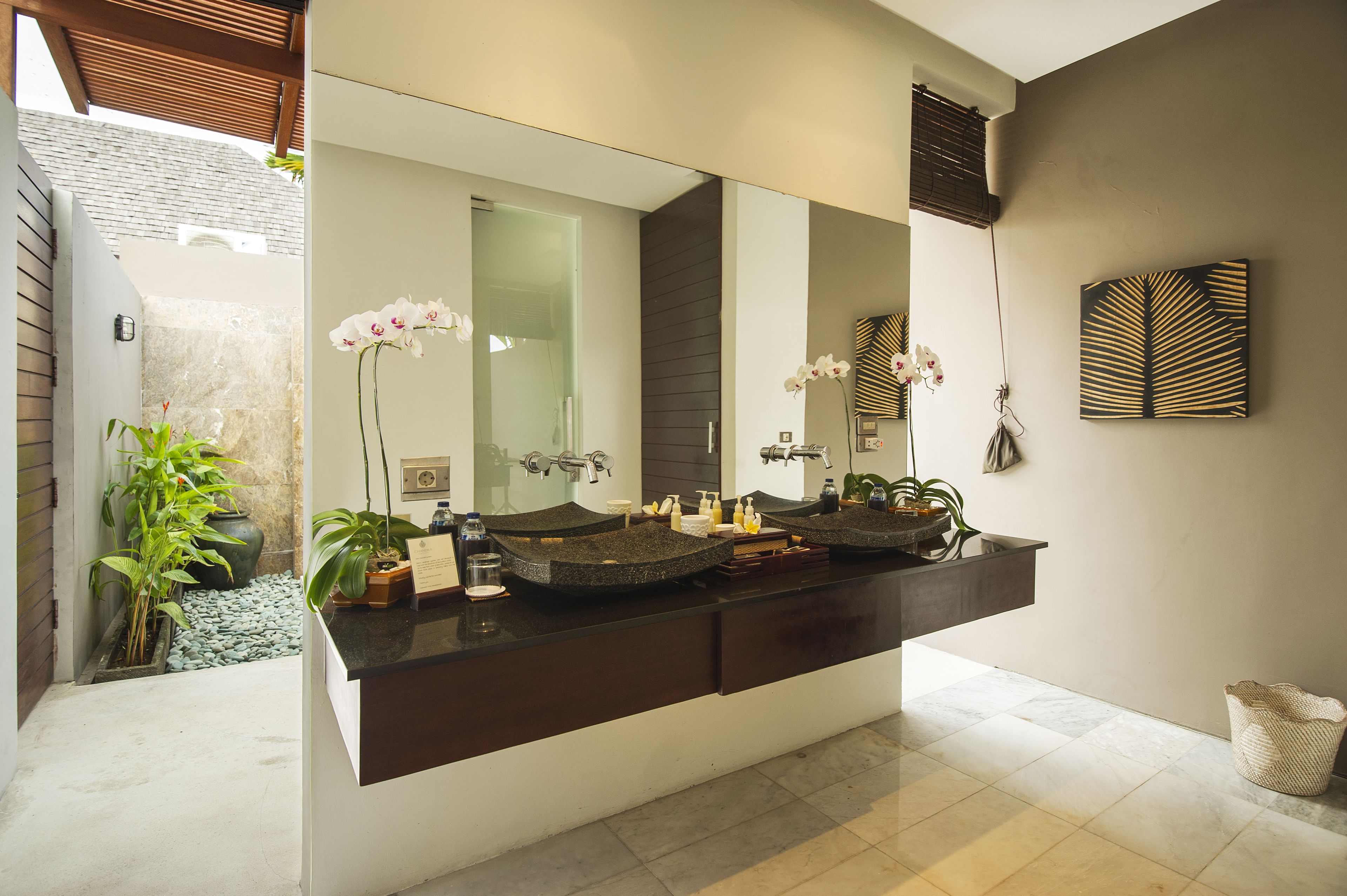 A modern bathroom with a large mirror, two sinks, and decorative plants.