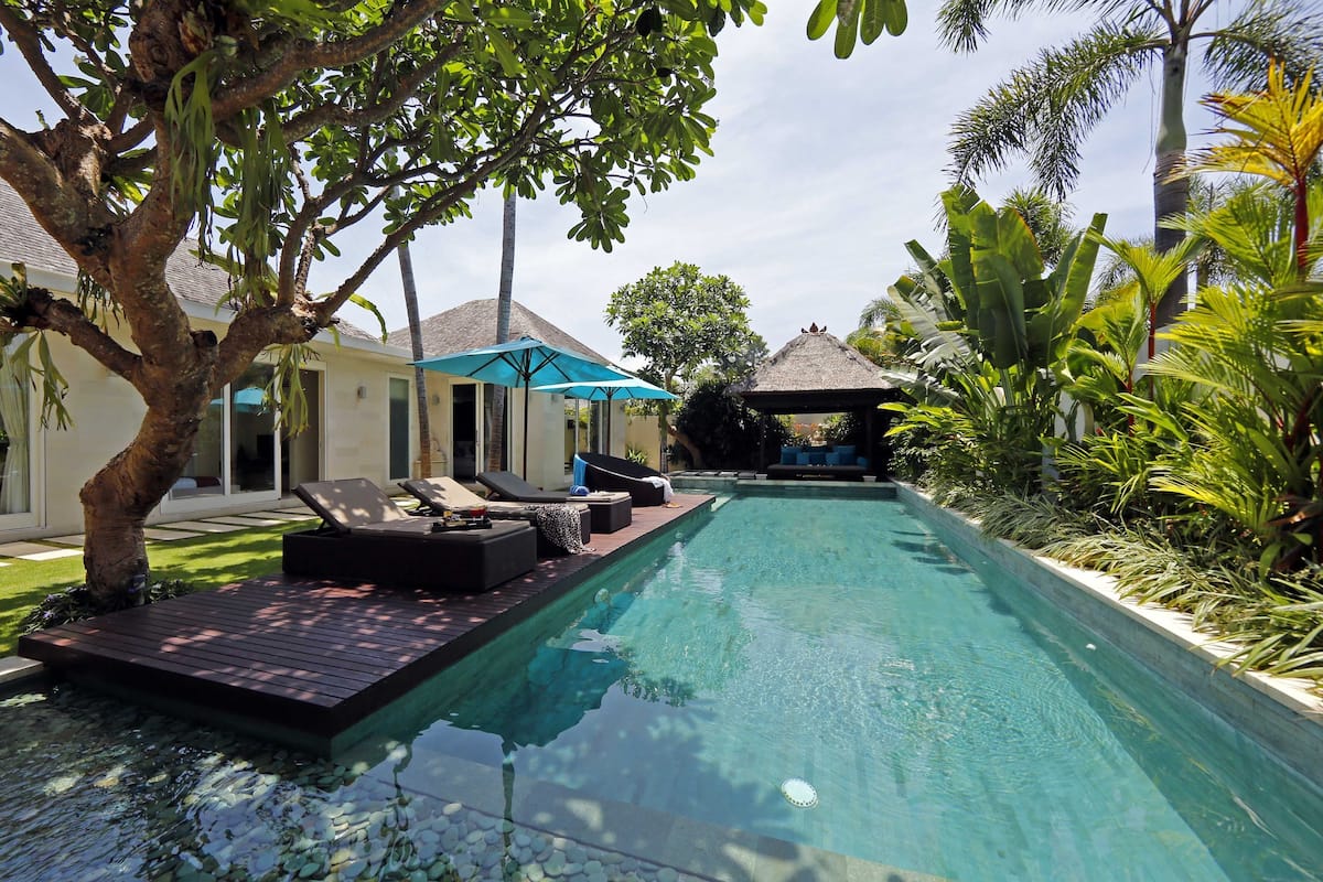 A swimming pool with lounge chairs and a thatched-roof structure.