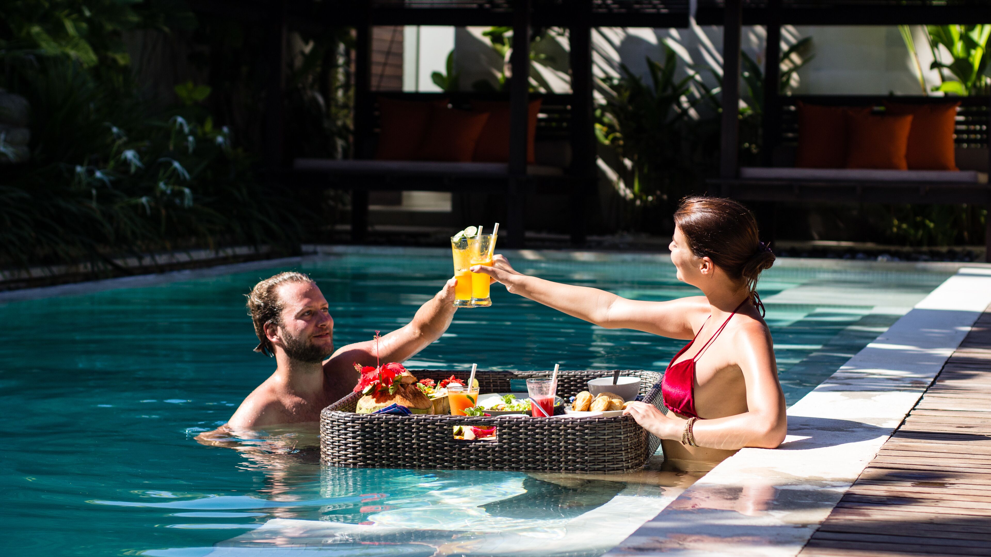 A couple in a swimming pool with a wicker basket containing food and drinks.