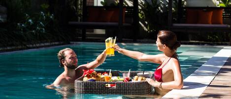 A couple in a swimming pool with a wicker basket containing food and drinks.