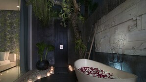 A spa area with a bathtub filled with rose petals, a potted plant, and candles along a pathway. - Chandra Bali Villas (Seminyak)