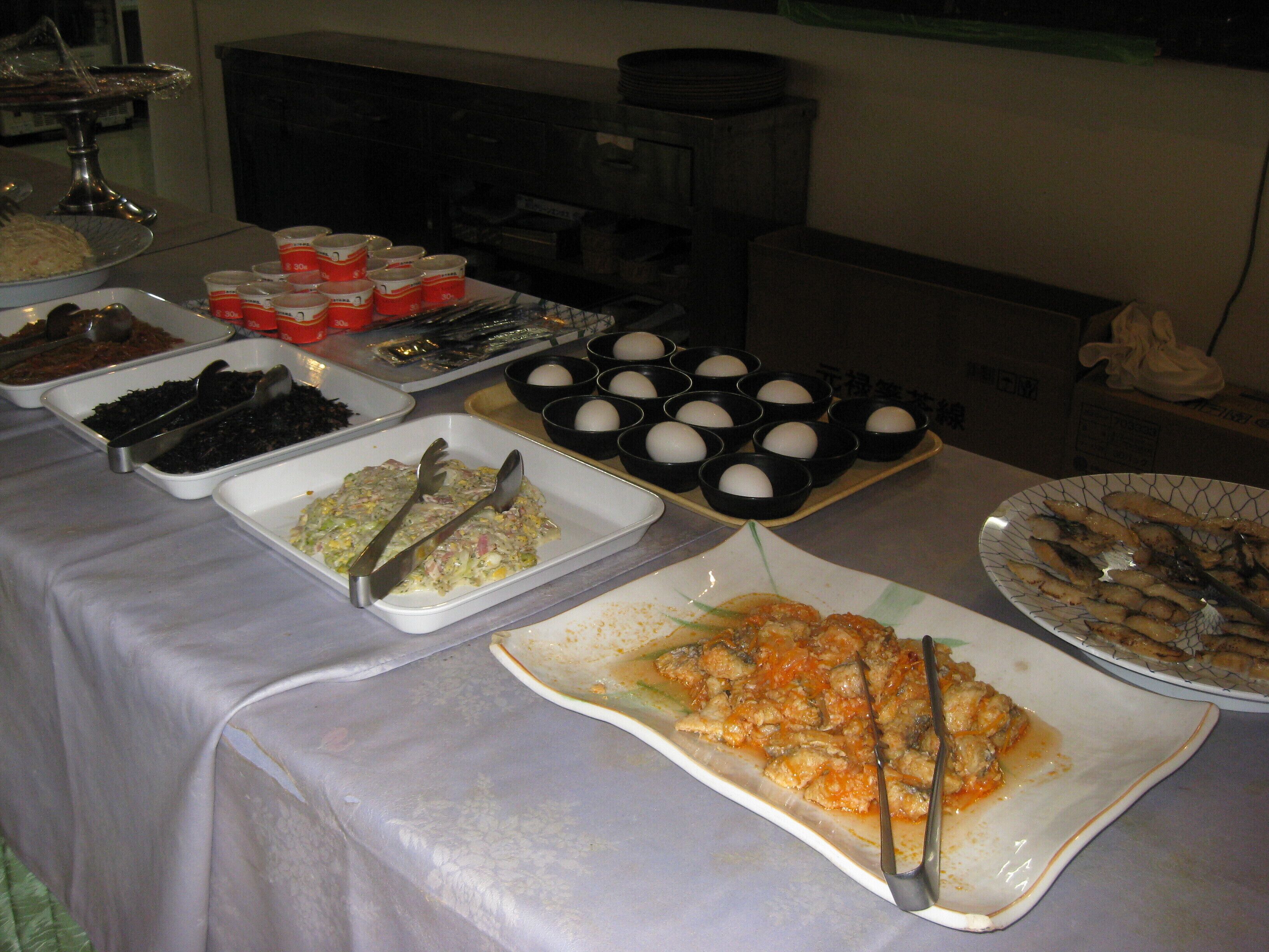 Una mesa de buffet con diferentes platos, incluyendo un guiso de pescado, una ensalada y varios recipientes con comida.