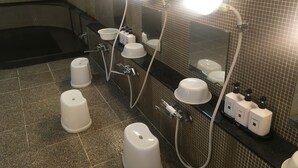 A bathroom with a large mirror, three illuminated lights, a bathtub, and three white urinals. - Tokyo Business Hotel (Tokyo)