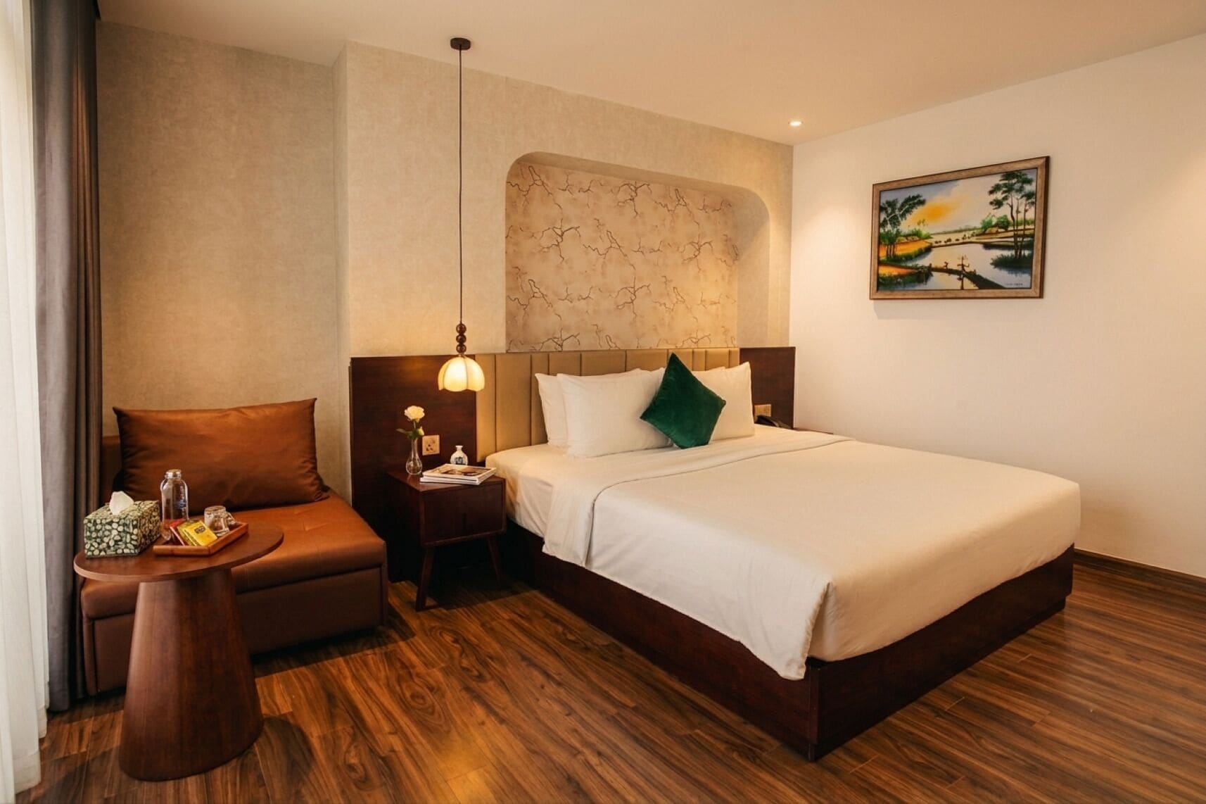 Une chambre d’hôtel avec un lit, une table de chevet, une lampe, une chaise et un tableau au mur.