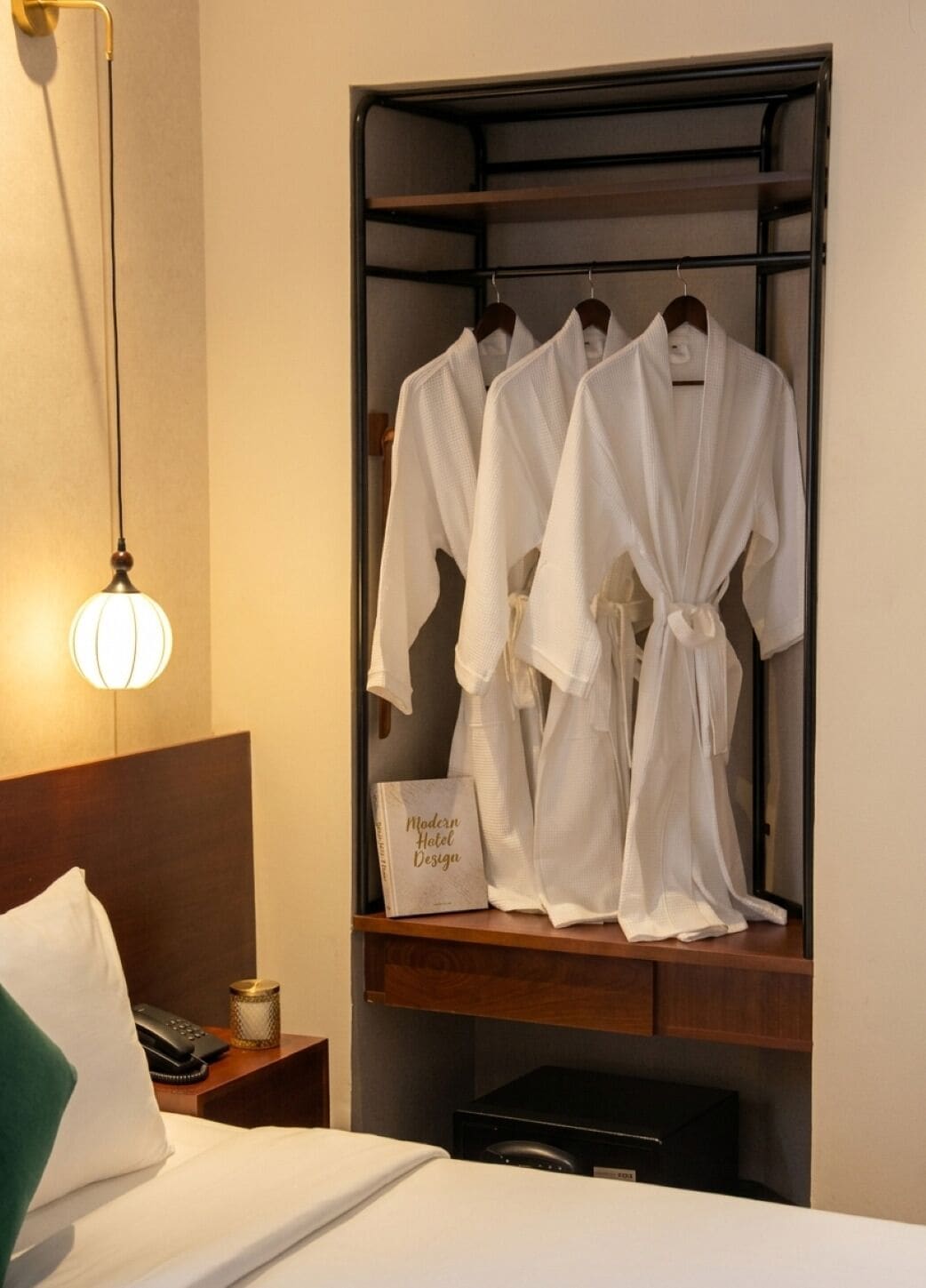 Ein Hotelzimmer mit Bett, Nachttisch mit Lampe, Kleiderständer mit Bademänteln und einem Buch mit dem Titel 'Modernes Hotdesign'.