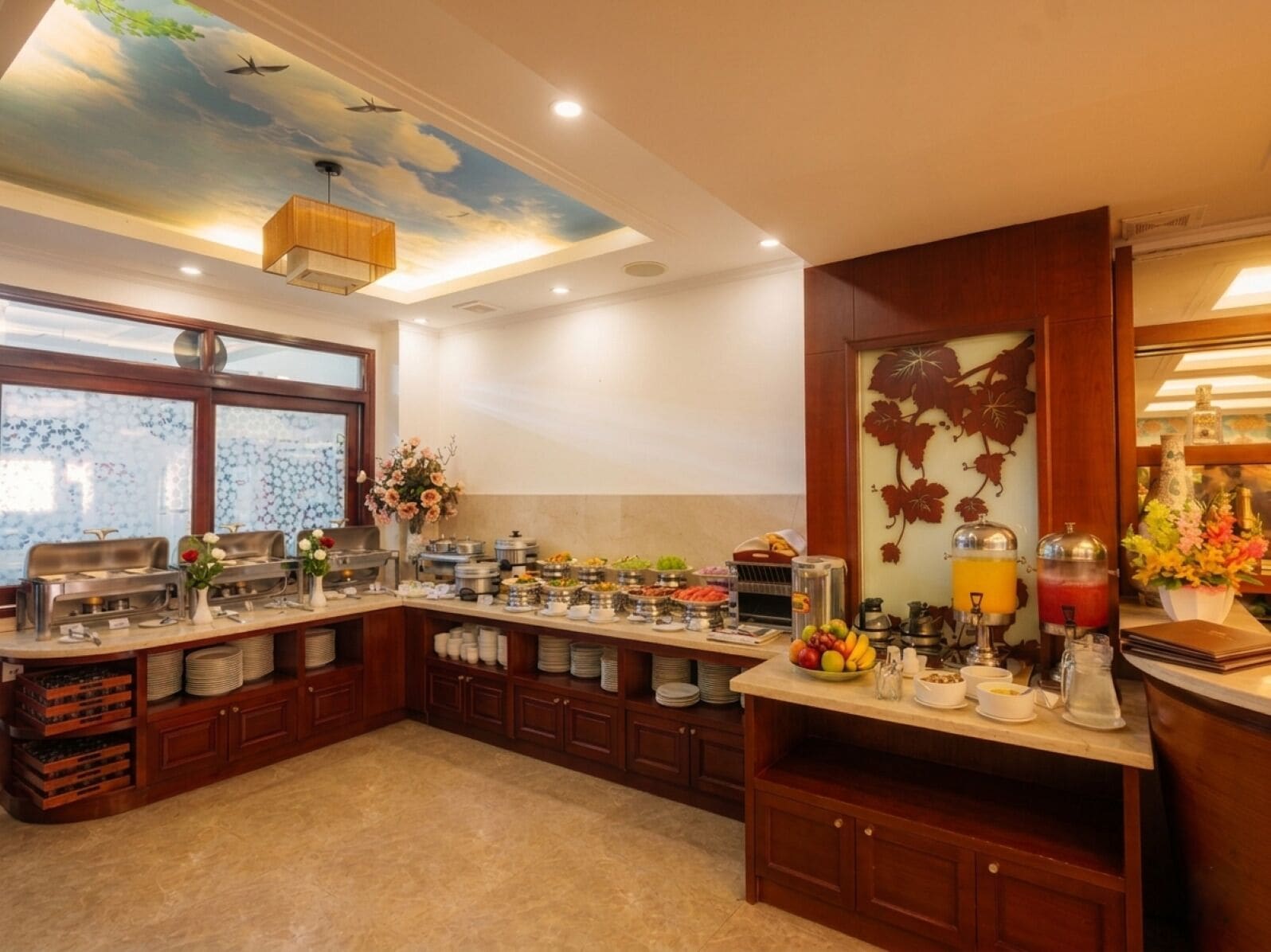 Cocina de hotel con mesa de buffet, que incluye distintas estaciones de comida y un mural en el techo.
