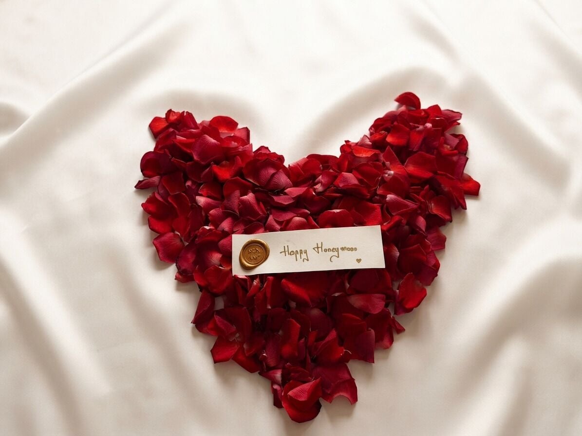 A heart-shaped arrangement of red rose petals with a wax seal and a card that reads 'Happy Honey Mood.'