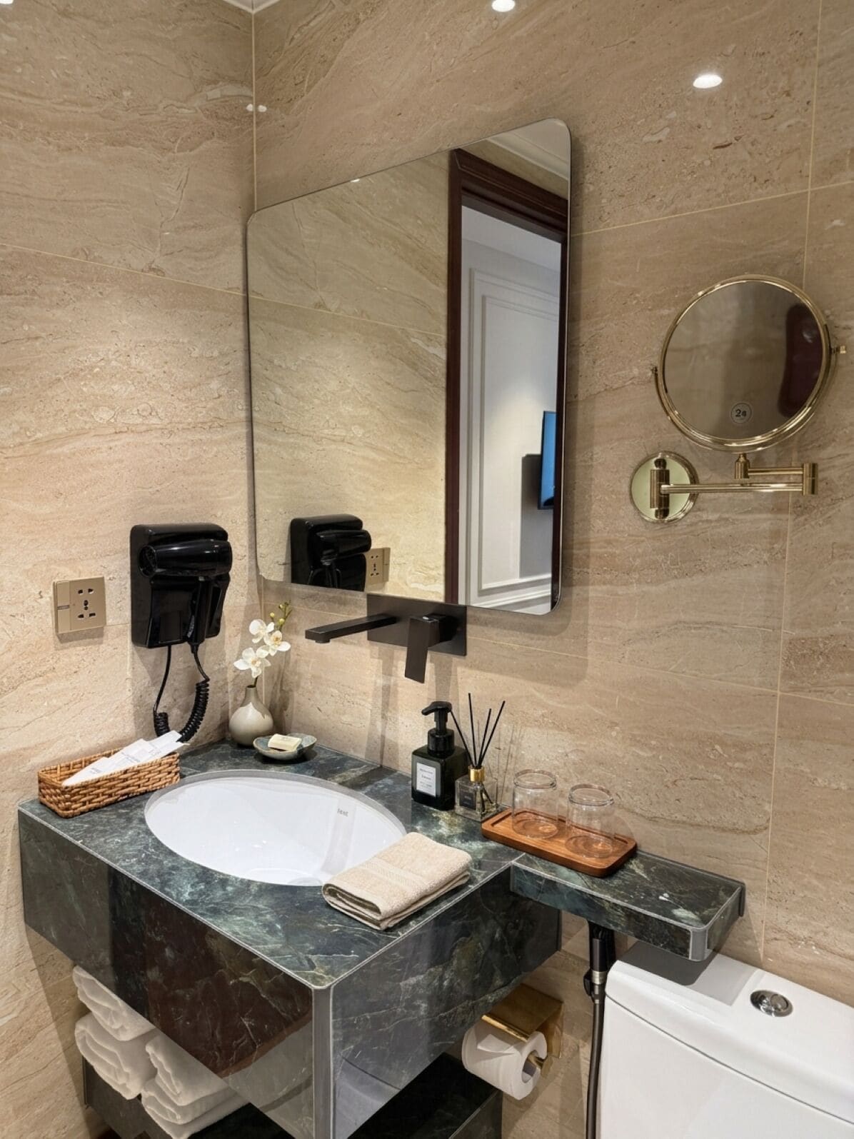 A modern bathroom with a marble sink, a large mirror, a toilet, and a wall-mounted phone.