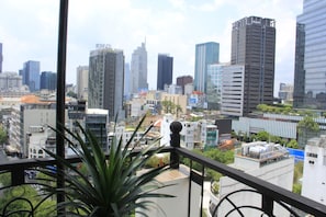 A cityscape with modern high-rise buildings, a balcony with a plant, and a clear view of the urban environment.