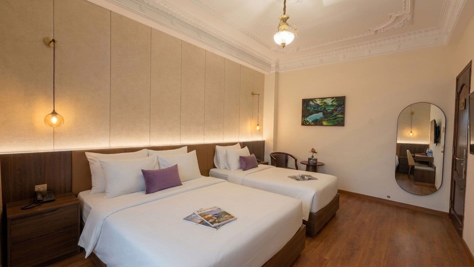 Une chambre d’hôtel avec deux lits, une table de chevet, une petite table, un miroir et un tableau au mur.