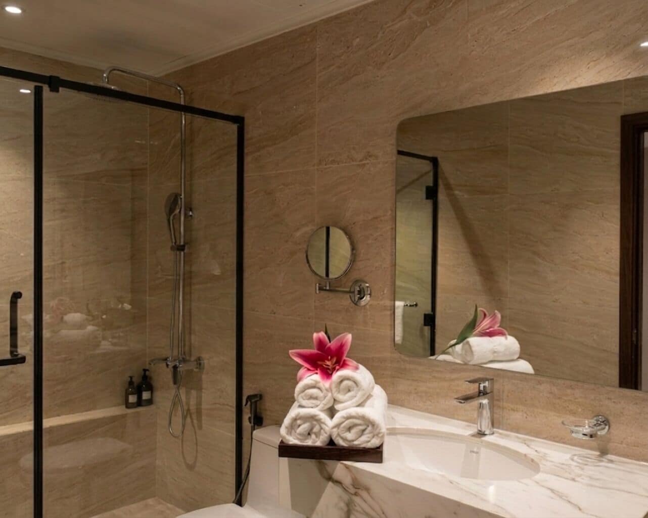 A modern bathroom with a glass shower enclosure, a marble sink, and a large mirror.