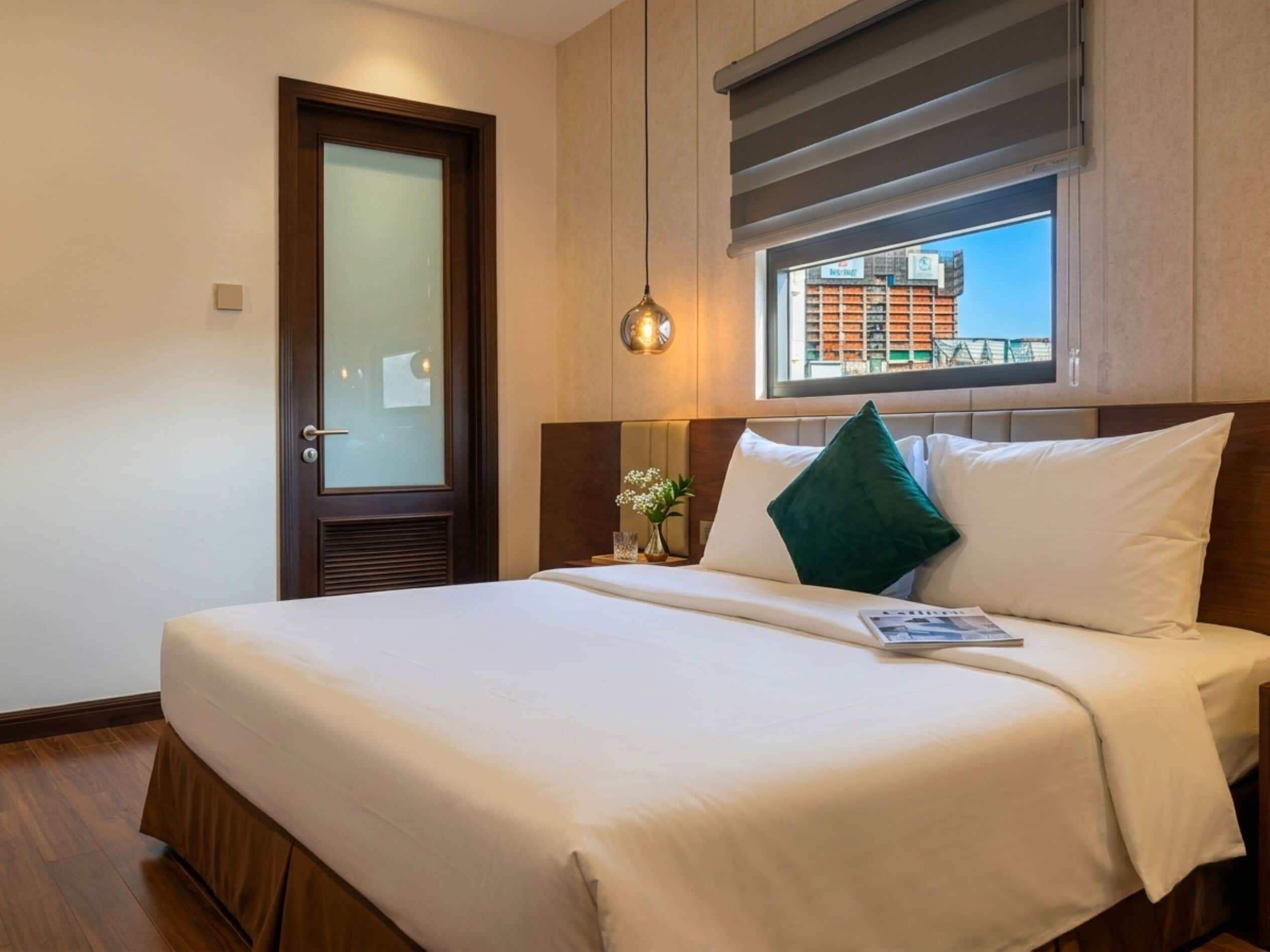Une chambre d’hôtel avec un grand lit, une fenêtre donnant sur un beau paysage, une porte en verre dépoli et une lampe de chevet.