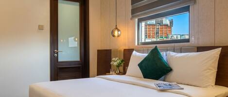 A hotel room with a large bed, a window with a view, a door with frosted glass, and a bedside lamp.