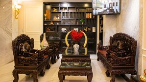 Een luxueuze lobby met versierde houten meubels, een centrale salontafel en een aan de muur bevestigde televisie.