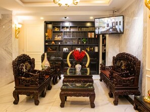 Um hall luxuoso com mobiliário de madeira ornamentado, uma mesa de centro e uma televisão fixada na parede.
