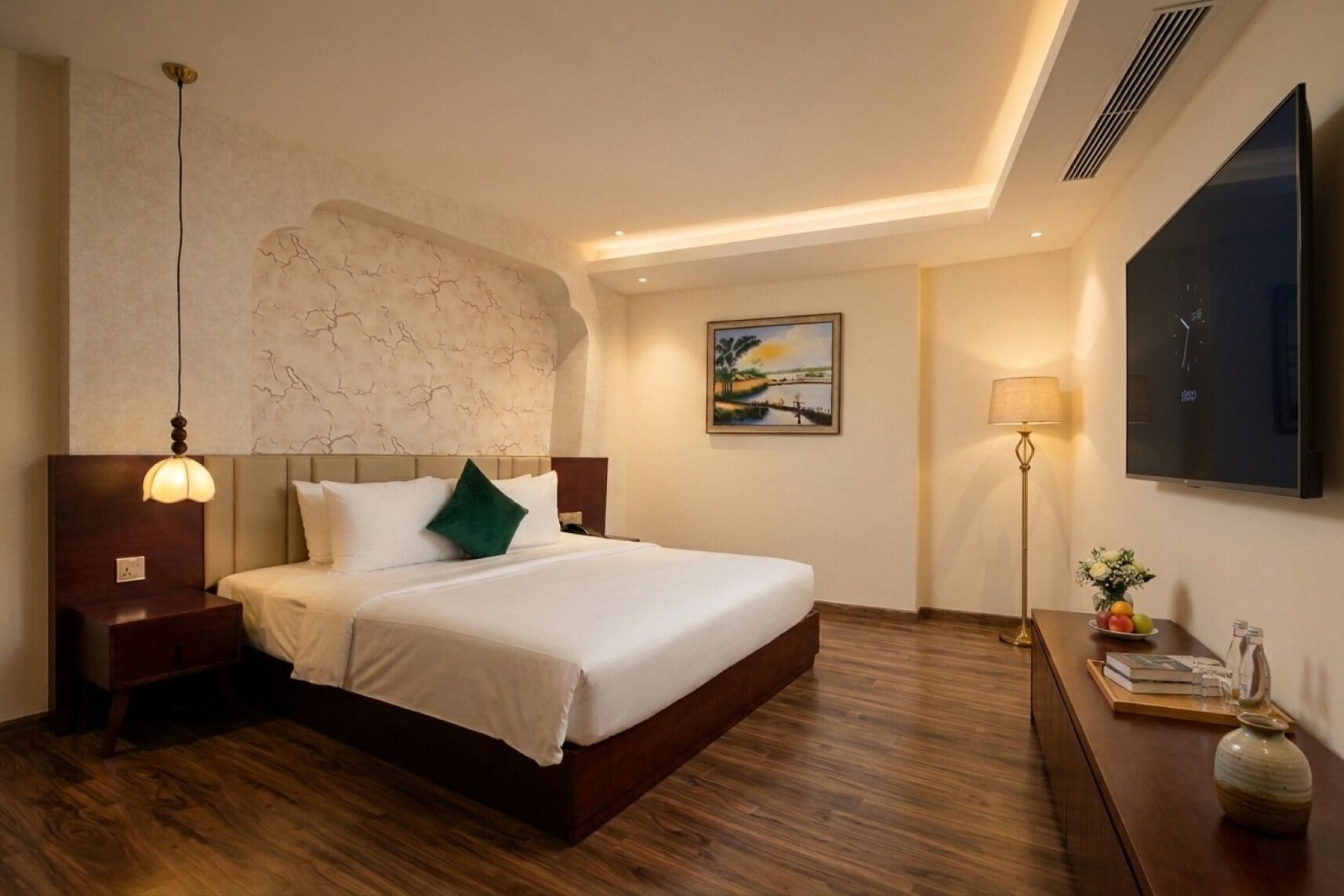 A hotel room with a bed, a nightstand, a wall-mounted TV, a painting, and a floor lamp.