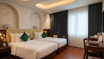 Een hotelkamer met twee bedden, een bureau en een groot raam met gordijnen.
