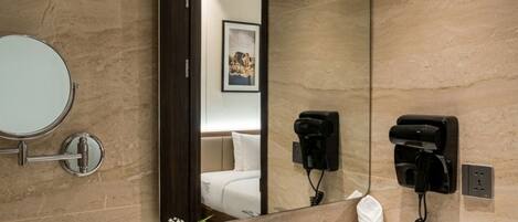 A bathroom with a marble sink, a large mirror, a hairdryer, and a towel rack.