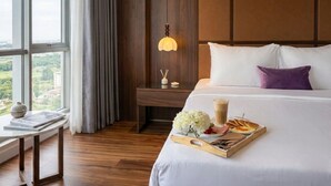 Een hotelkamer met een groot bed, een nachtkastje met lamp, een dienblad met ontbijtartikelen en een raam met uitzicht op groen.