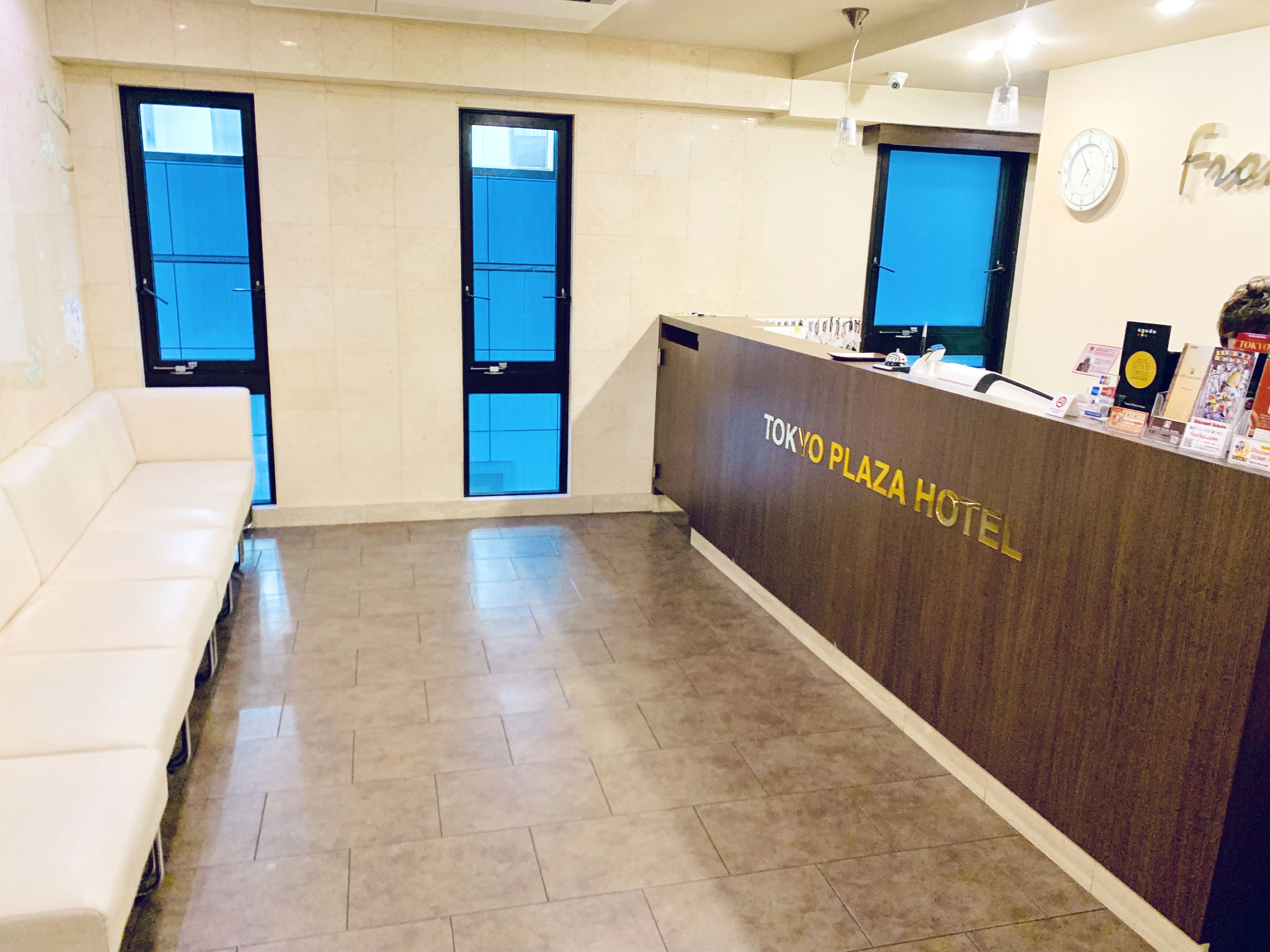 A reception area with a reception desk labeled "TOKYO PLAZA HOTEL," two windows, a clock, and a seating area.