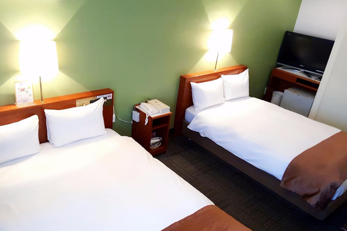 Habitación de hotel con dos camas, un televisor y un escritorio pequeño con teléfono.