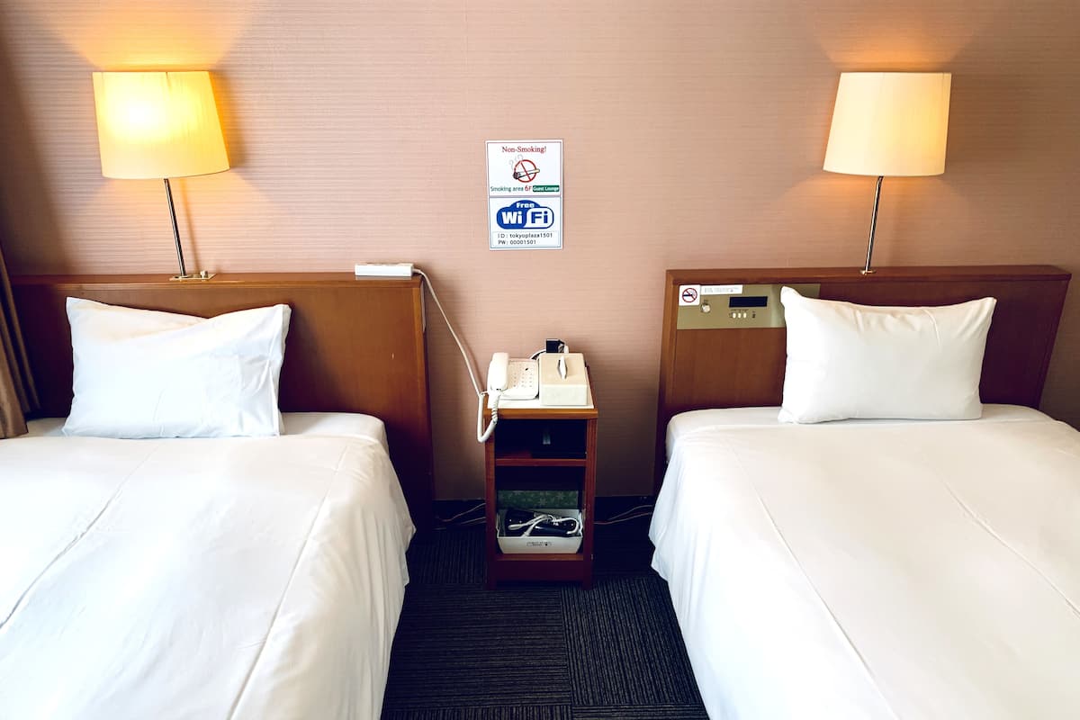 Habitación de hotel con dos camas, cada una con ropa blanca, una mesita de noche con teléfono y lámpara, y un letrero que indica zona para no fumadores y Wi-Fi gratuito.