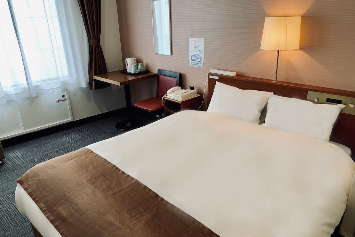 Habitación de hotel con una cama grande, un escritorio con teléfono, una silla y una lámpara.