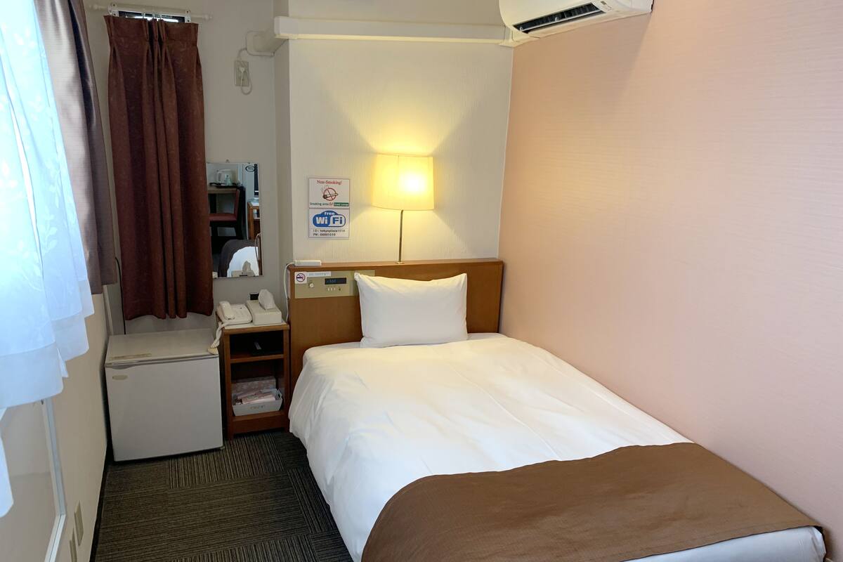 Habitación de hotel con una cama, un escritorio con teléfono, una lámpara y un cartel que indica zonas para no fumadores.