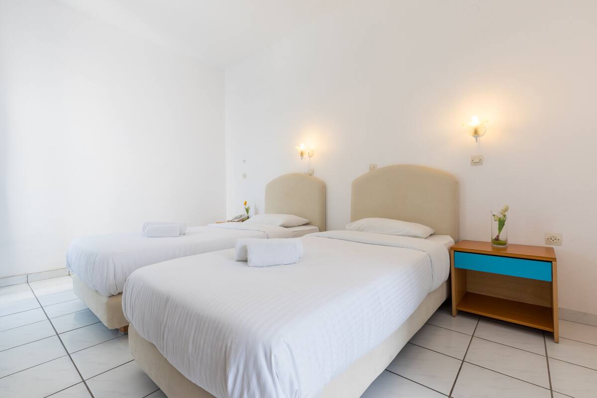 Habitación de hotel con dos camas, una mesita de noche y luces fijadas a la pared.