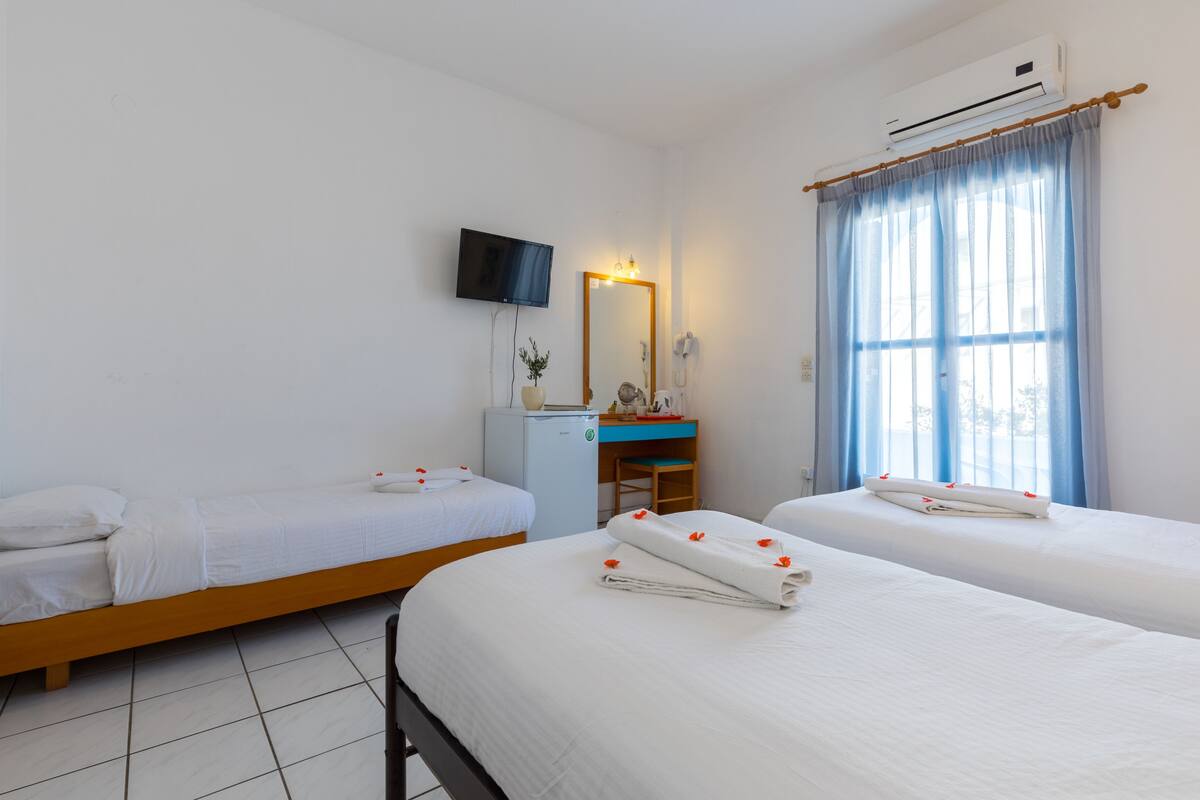 Habitación de hotel con dos camas individuales, un escritorio pequeño con una silla, un televisor montado en la pared y un equipo de aire acondicionado.