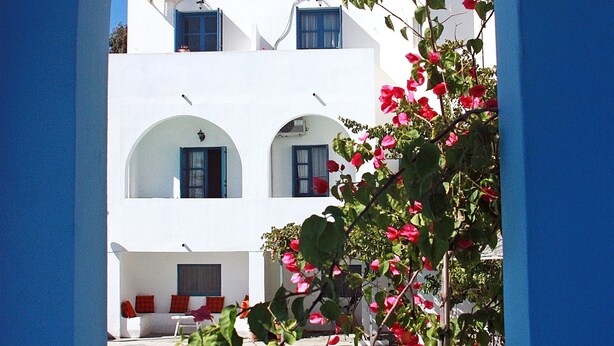 A white building with blue accents, a pool, and a view through an archway.