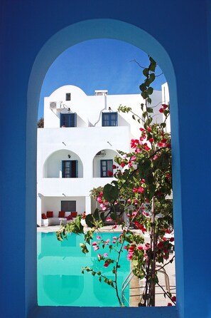 A white building with blue accents, a pool, and a view through an archway. - Hotel Kalma (Santorini)
