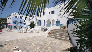 A white building with blue accents, a stone courtyard, and outdoor seating.