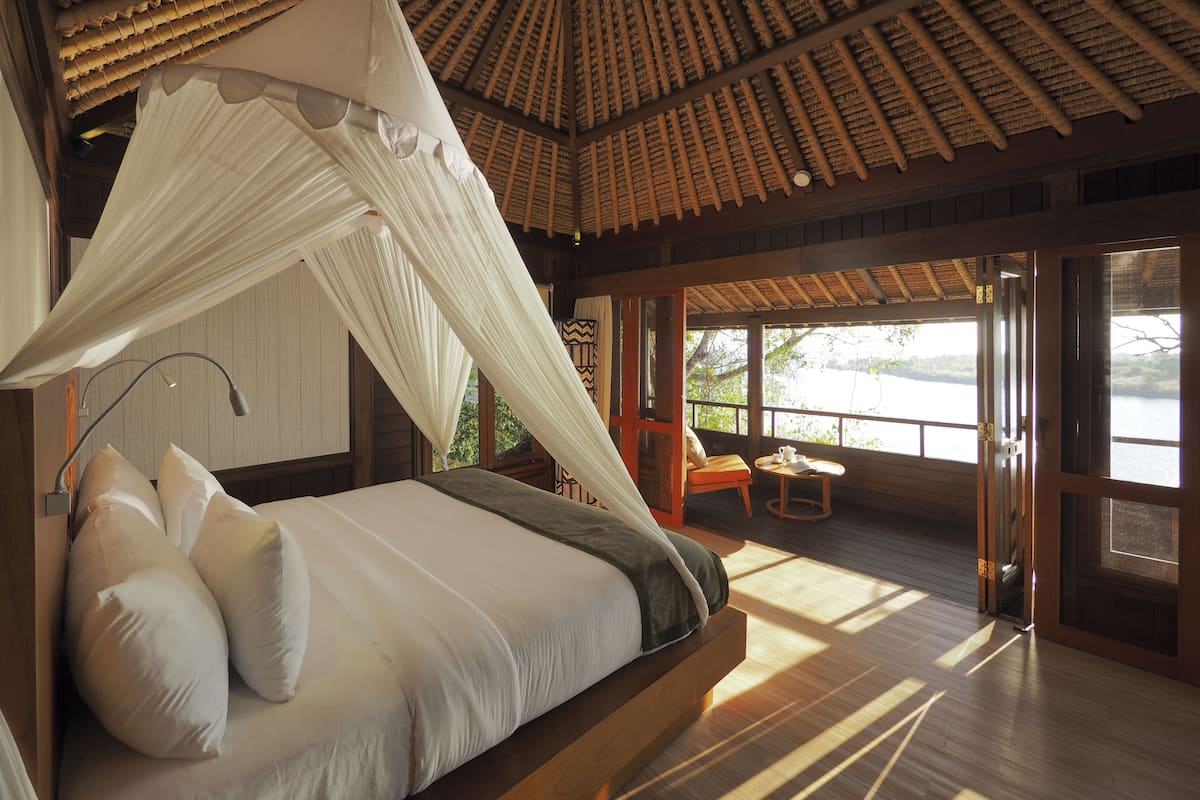 A room with a bed, a canopy, a view of a body of water, and a wooden floor.