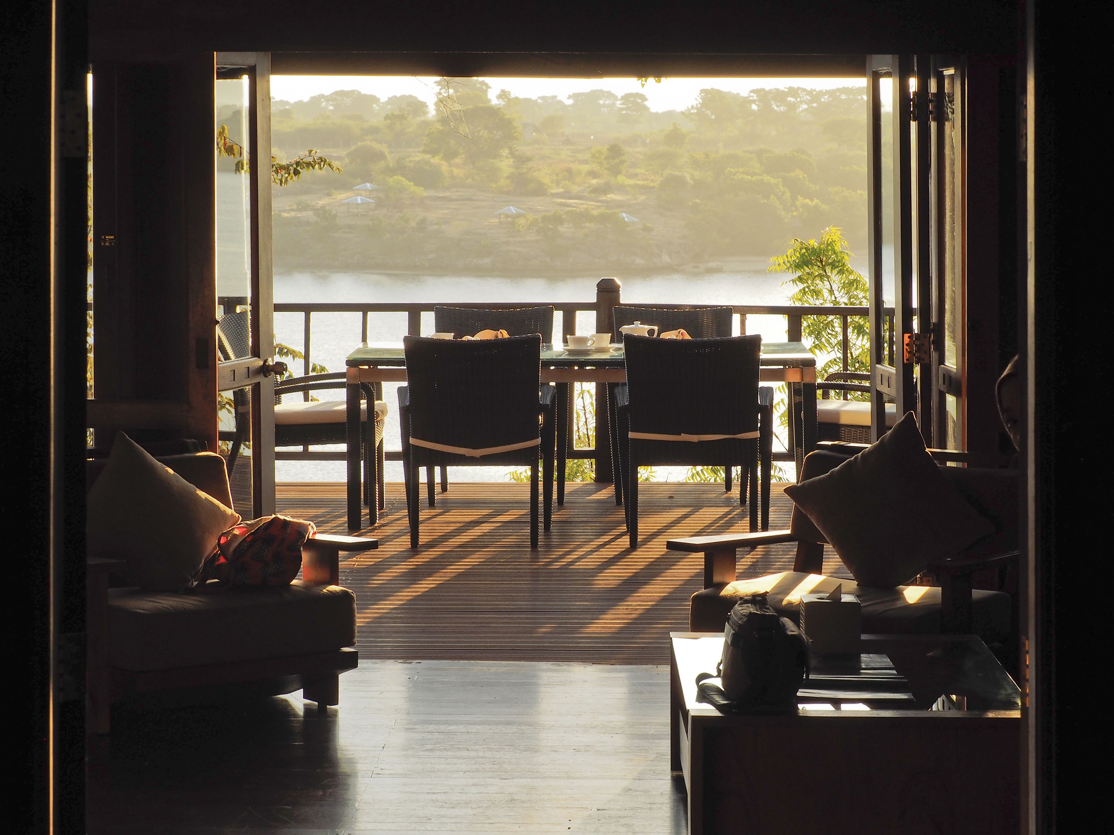 A room with a view of a lake, furnished with a table and chairs, and a sofa.