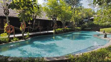 Relax by the serene pool surrounded by lush greenery and traditional structures.