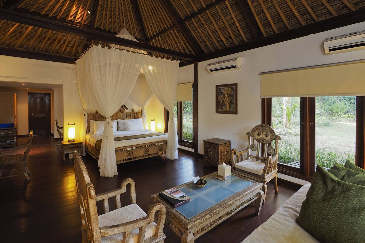 A spacious room with a large bed, a sitting area with a coffee table, and a view of the outdoors.