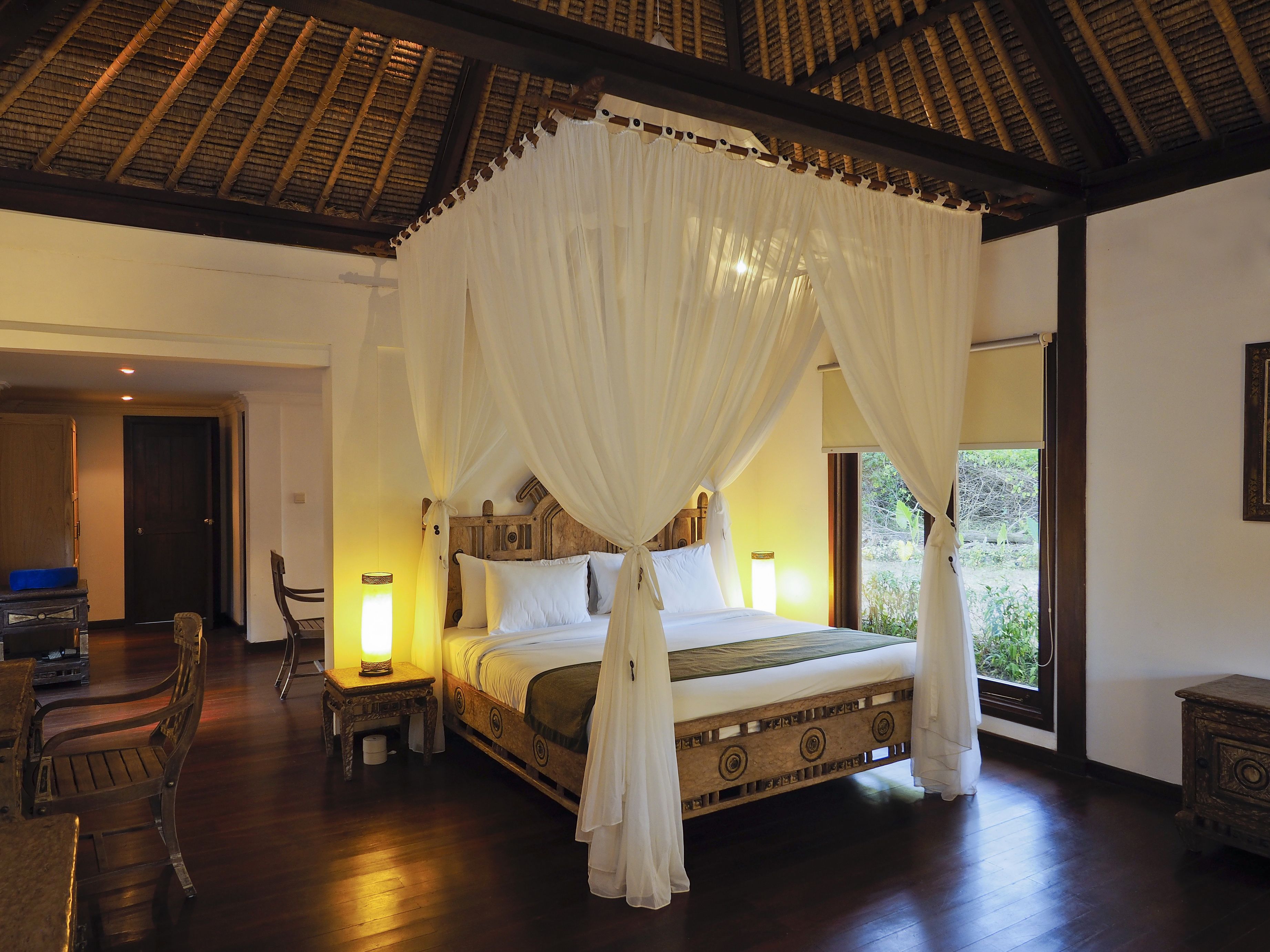 A room with a four-poster bed, wooden furniture, and a thatched roof ceiling.
