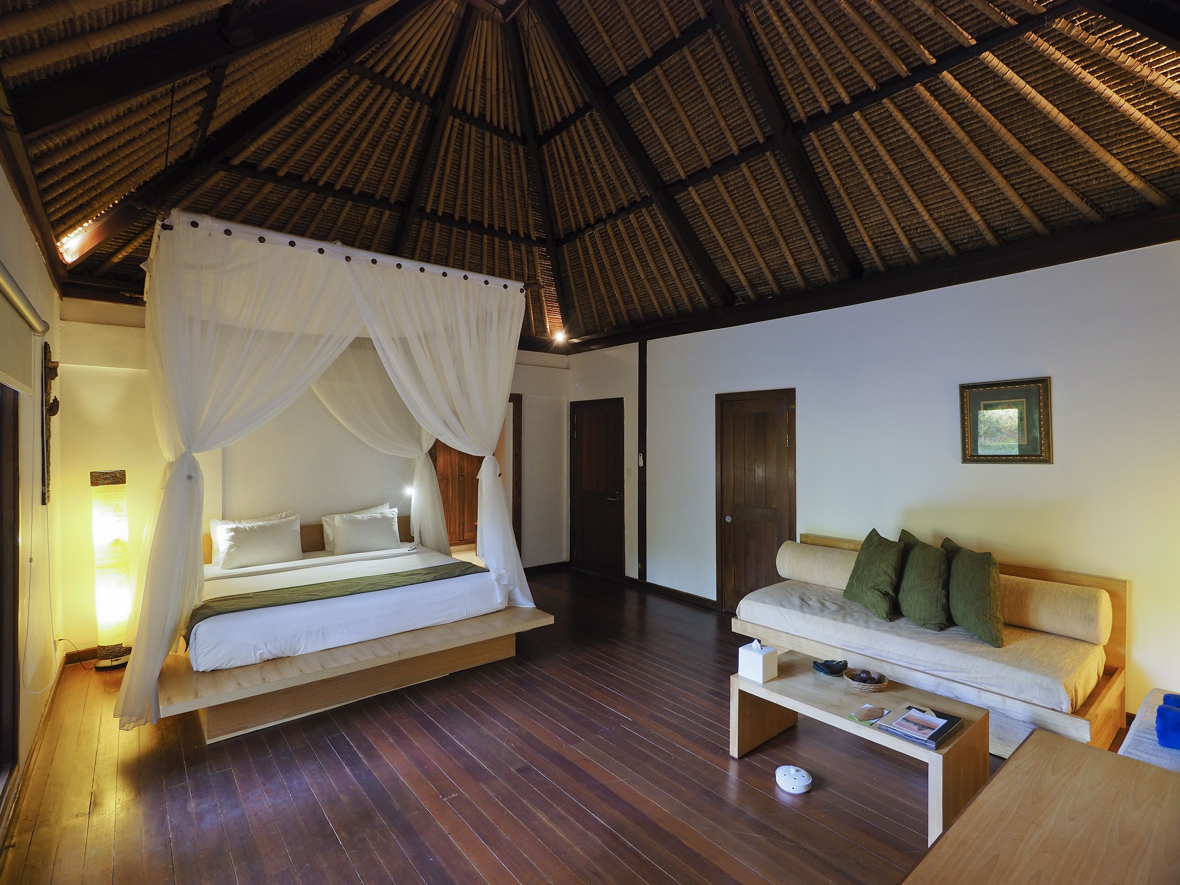 A room with a bed under a canopy, a sofa, a wooden coffee table, and a framed picture on the wall.