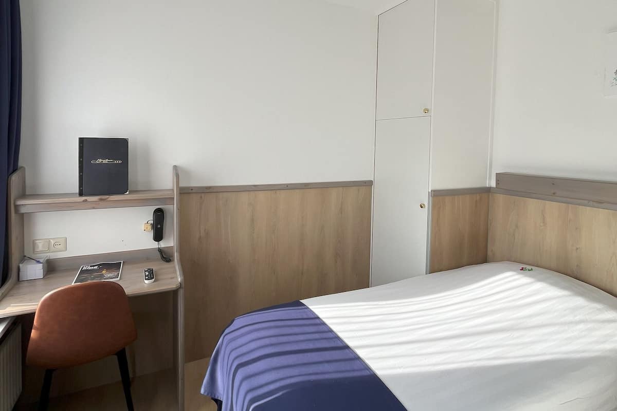 A hotel room with a bed, a desk, a chair, a wardrobe, and a telephone.