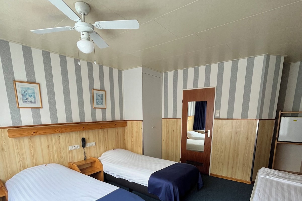 A hotel room with two beds, a ceiling fan, a wooden headboard, a small desk with a telephone, and a mirror.