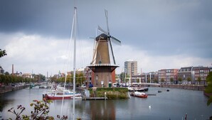 Ein Kanal mit Windmühle und Booten, umgeben von Gebäuden und einer Brücke.