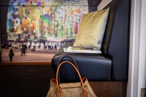 Ein schwarzes Ledersofa mit Kissen und Zeitschrift, eine braune Lederhandtasche und ein farbenfrohes Wandbild im Hintergrund.