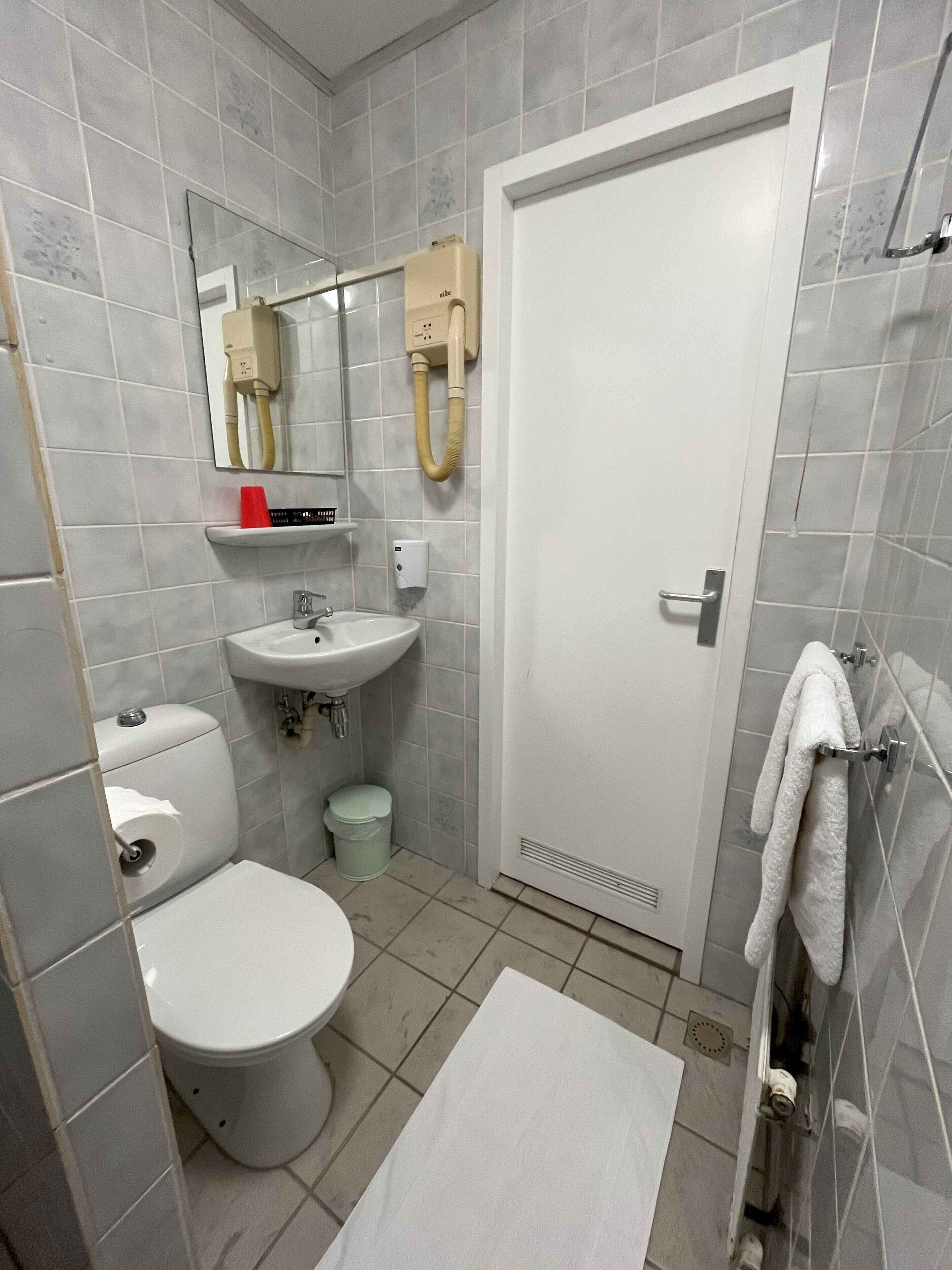 A bathroom with a toilet, sink, mirror, and towel rack.