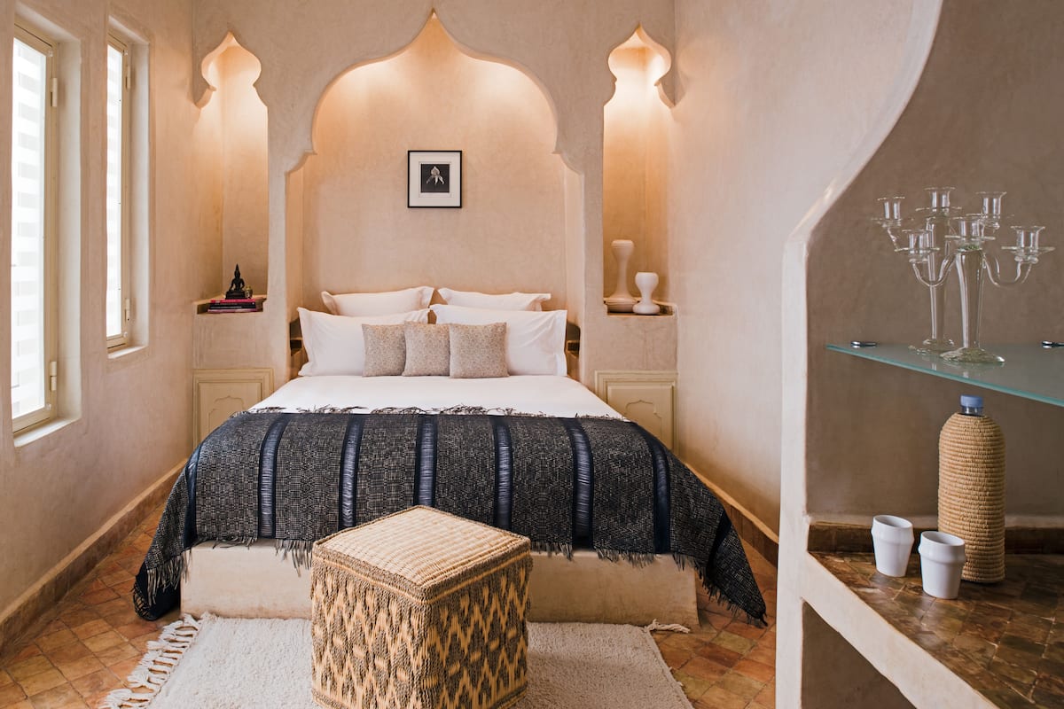 A bedroom with a large bed, a small side table, a decorative wall arch, and a glass shelf with candles.