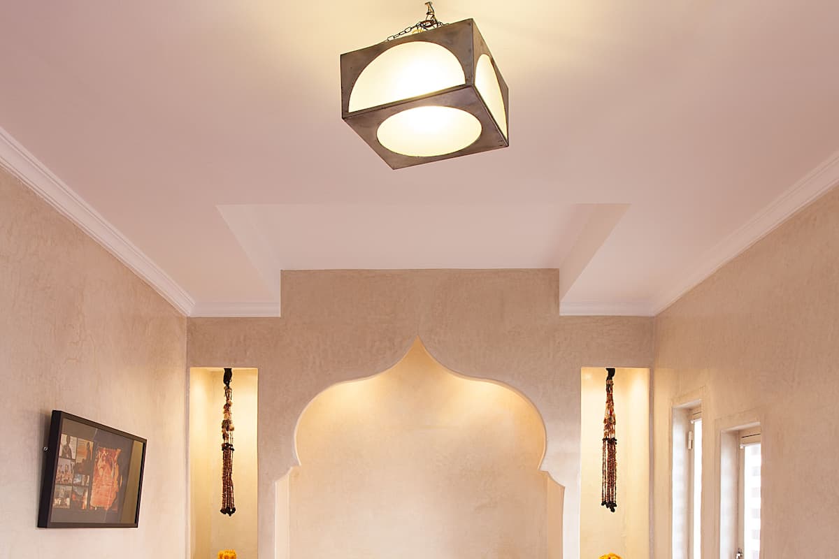 A bedroom with a bed, two purple chairs, a round table, and a hanging light fixture.