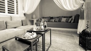 A living room with a sofa, a coffee table with a tray of pastries, a decorative lamp, and a patterned rug. - Riad Cocoon (Marrakech)