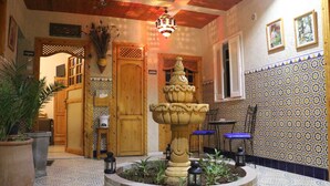 A courtyard with a stone fountain, wooden doors, tiled walls, and potted plants. - Riad les Chtis d'Agadir (Agadir)