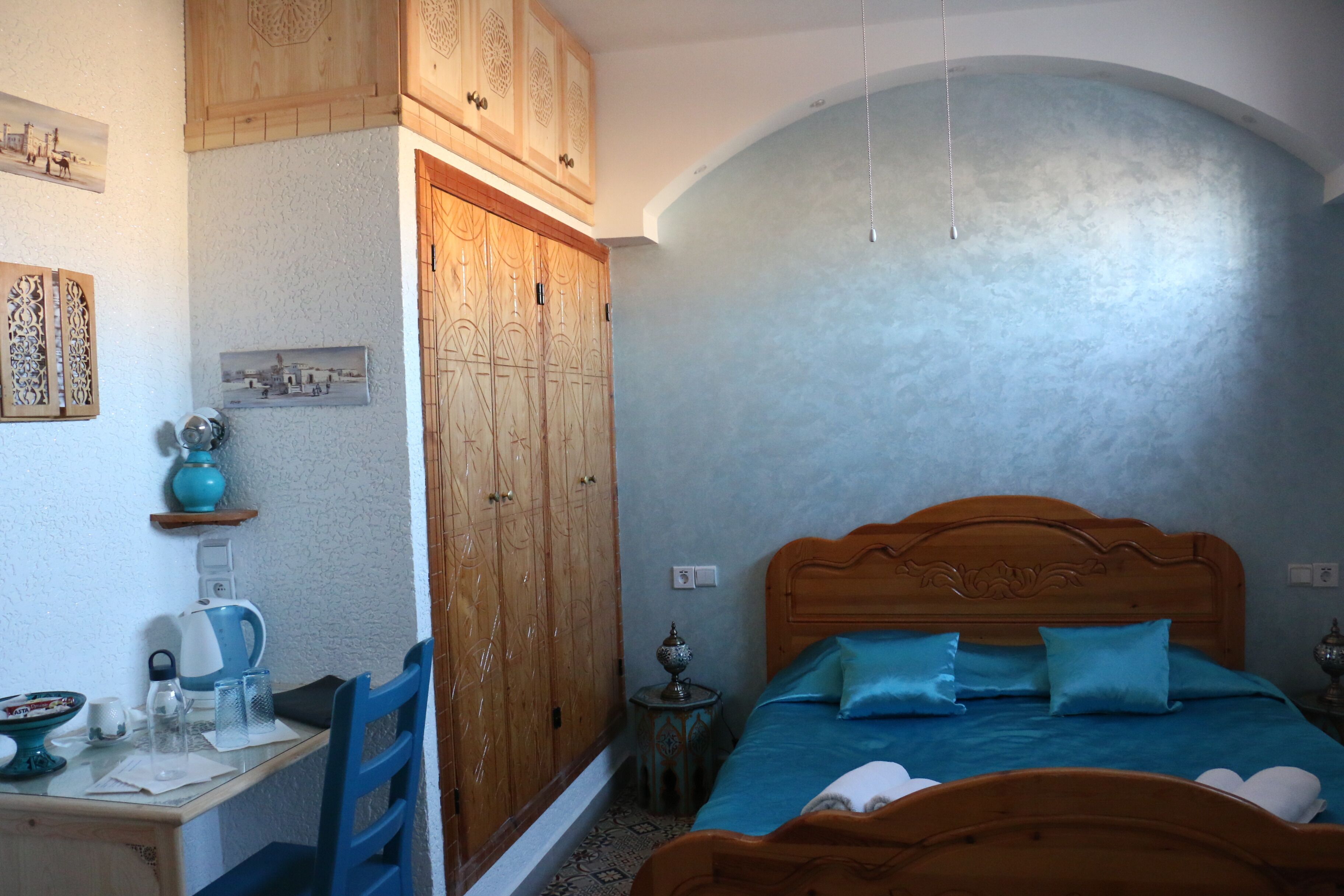 A bedroom with a wooden bed, a desk with a kettle, and a wardrobe.