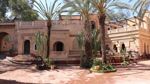 A courtyard with palm trees, a fountain, and a building with arches and patterned walls. - Riad les Chtis d'Agadir (Agadir)